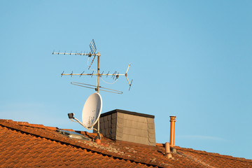 tv antenna and satellite dish on an old house roof