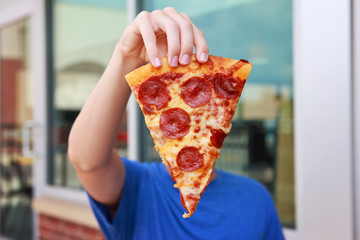 Boy holding a piece of pepperoni pizza in front of his face