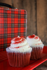 Red velvet cupcakes with a vintage plaid metal lunchbox on a wooden background