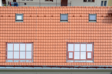The roof of the house with red tiles and windows of mansard