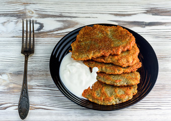 potato pancakes with sour cream, on a black plate on a wooden background. Home kitchen.