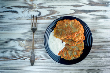 potato pancakes with sour cream, on a black plate on a wooden background. Home kitchen.