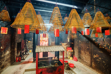 Minor Buddhist temple interior in historic center of Macau. Burning incense prayer cones and a censer