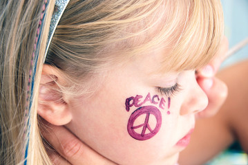 little blond girl with face painted peace sign on cheek