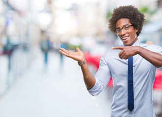 Afro american business man wearing glasses over isolated background amazed and smiling to the camera while presenting with hand and pointing with finger.