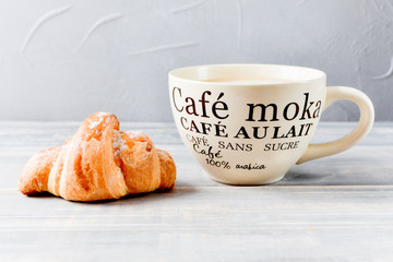 large beige Cup of coffee with milk and croissants on a wooden table. on the Cup inscription in French (top down: mocha coffee, coffee with milk, coffee without sugar)