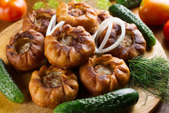 Fried meat pies belyash with vegetables on wooden board