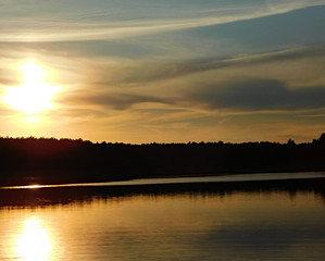 A beautiful photo of the sunset at the lake, with rays reflecting in the water and a dark line of trees