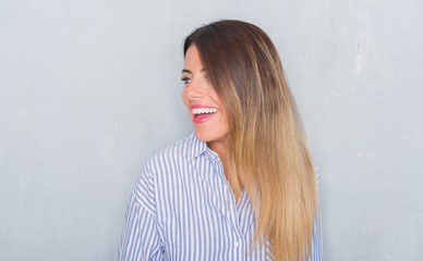 Fototapeta premium Young adult woman over grunge grey wall wearing business shirt looking away to side with smile on face, natural expression. Laughing confident.