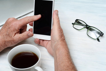 Top view of old man hand holding a cup of coffee and smartphone