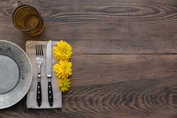 Rustic table setting with linen napkin, cutlery, ceramic plates, yellow glasses and yellow flowers