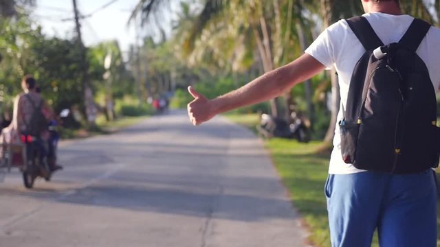 A man with a backpack behind him goes along the road, catches a vehicle, holding up his hand, a camera with movement. slow motion, HD, 1920x1080