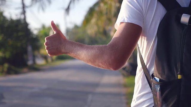 A man with a backpack behind him goes down the road at sunset, catches a vehicle, holding up his hand, a camera with movement. slow motion, HD, 1920x1080