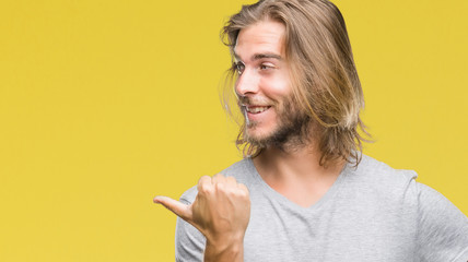 Young handsome man with long hair over isolated background holding football ball pointing and...