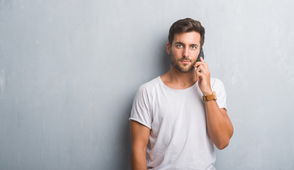 Handsome young man over grey grunge wall speaking on the phone with a confident expression on smart...