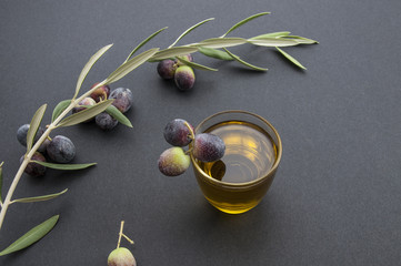 olive oil in a glass olive tree branch and olives on a black background