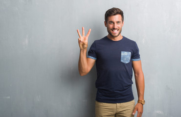 Handsome young man over grey grunge wall showing and pointing up with fingers number three while...