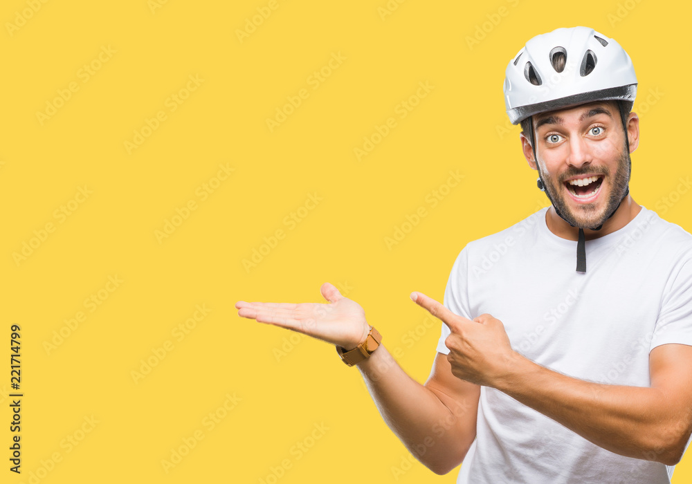 Wall mural Young handsome man wearing cyclist safety helmet over isolated background amazed and smiling to the camera while presenting with hand and pointing with finger.