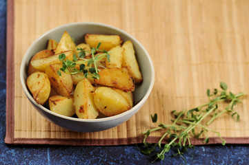 Slices of fried potatoes in a deep bowl. Potatoes are supplemented with sprouts of green peas. The background is a napkin made of bamboo. Close-up. 