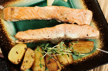 Steak of salmon and slices of fried potatoes on a square plate. On a plate, greens from pea shoots. Plate with fish occupies the entire frame space. View from above. Close-up. Macro photography.