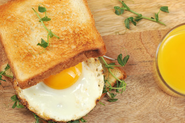 Toast with fried egg and sprouts of peas on a wooden tray. Close to a glass of orange juice. Light background. Close-up. View from above. Macro photography.