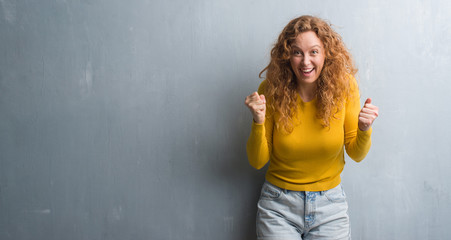 Fototapeta premium Young redhead woman over grey grunge wall screaming proud and celebrating victory and success very excited, cheering emotion