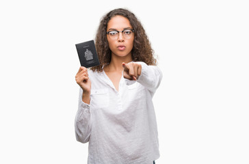 Young hispanic woman holding passport of Canada pointing with finger to the camera and to you, hand sign, positive and confident gesture from the front