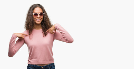 Beautiful young hispanic woman wearing sunglasses looking confident with smile on face, pointing oneself with fingers proud and happy.