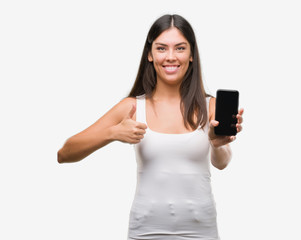 Fototapeta premium Young beautiful hispanic showing smartphone happy with big smile doing ok sign, thumb up with fingers, excellent sign