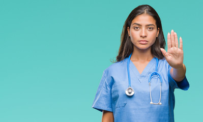 Young arab doctor surgeon woman over isolated background doing stop sing with palm of the hand....