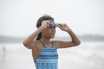 Beautiful curly haired mixed race pre-teen child in swim wear putting on her swimming goggles