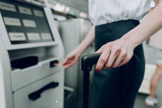 Close up of female hand is holding suitcase, while inserting bank card into cash dispenser