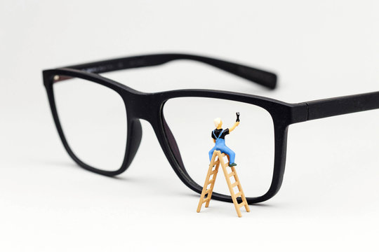 Miniatur Fensterputzer reinigt Glas einer Brille 