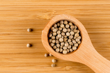 White peppercorn in wooden spoon, close up isolated on wood background