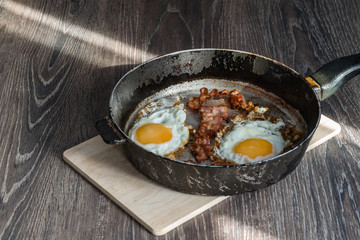 fried eggs with bacon in a frying pan are on the table