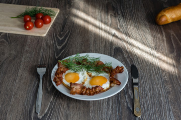 fried eggs with bacon and dill on a plate are on the table with tomatoes and bread