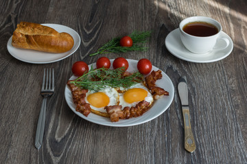 fried eggs with bacon and dill on a plate are on the table with tomatoes and bread