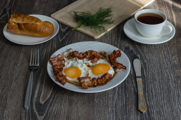 fried eggs with bacon and dill on a plate are on the table with tomatoes and bread