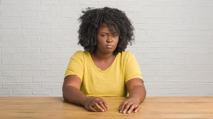 Fototapeta premium Young african american woman sitting on the table at home skeptic and nervous, frowning upset because of problem. Negative person.