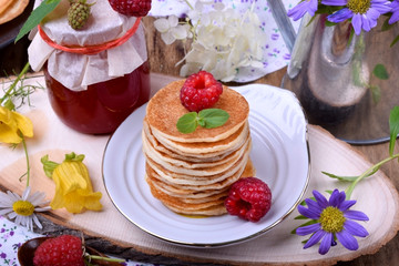 Stack of pancakes decorated with raspberry and mint on a white plate. Village style