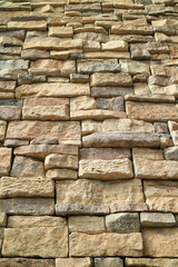 Low angle of brown and gray rough stone wall, vertical photo for background
