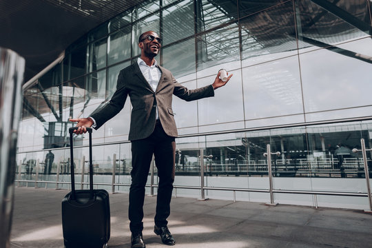 Happy about journey. Full length portrait of man during his business trip. He stands at the airport holding case and cup of coffee