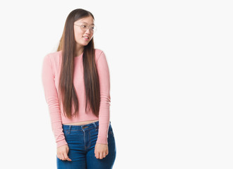 Young Chinese woman over isolated background wearing glasses looking away to side with smile on face, natural expression. Laughing confident.