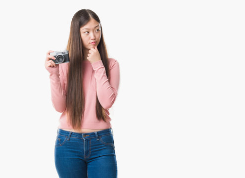 Young Chinese woman over isolated background taking pictures using vintage camera serious face thinking about question, very confused idea