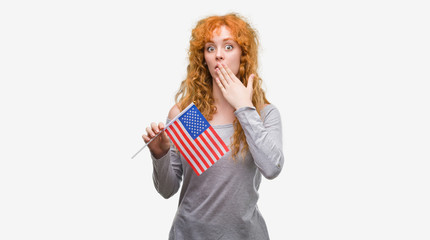 Young redhead woman holding flag of United States of America cover mouth with hand shocked with shame for mistake, expression of fear, scared in silence, secret concept