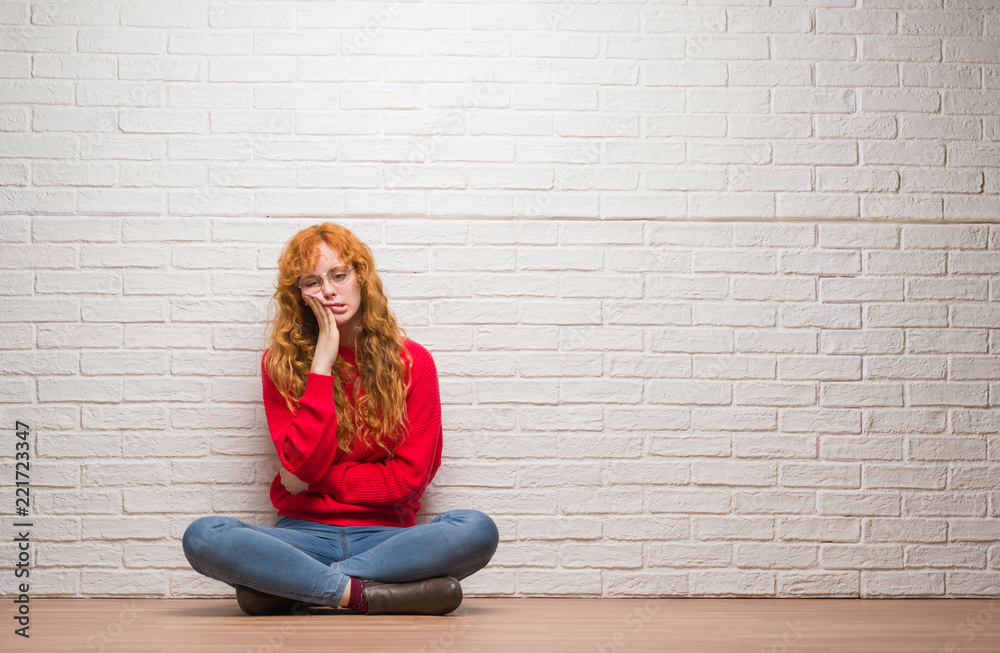 Poster young redhead woman sitting over brick wall thinking looking tired and bored with depression problem