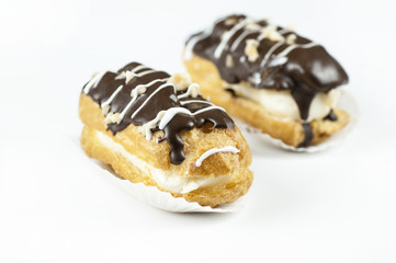 Eclairs  with black chocolate and white chocolate with hazelnut and custard on white background and backdrop. Traditional French dessert