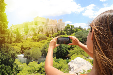 Cute young woman takes a picture of the Acropolis, Athens, Greece. Famous ancient Greek Acropolis is the main landmarks of Athens. Female tourist visits the Athens and takes a photo.