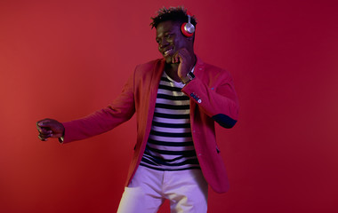Amazing track. Portrait of young gentleman in headphones enjoying favorite song and moving to the rhythm. Isolated on red background