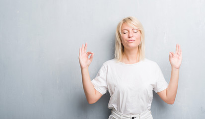 Adult caucasian woman over grunge grey wall relax and smiling with eyes closed doing meditation gesture with fingers. Yoga concept.